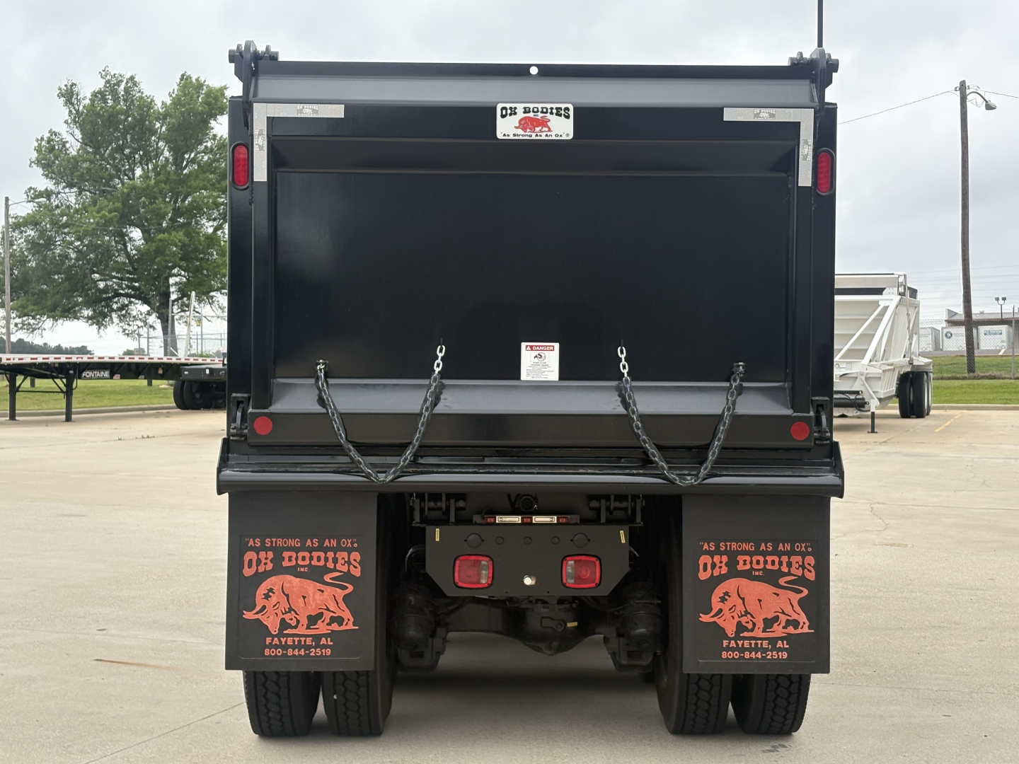 Dump truck bed showing rear view with tailgate chains and taillights, Mack branding and bumper area visible.