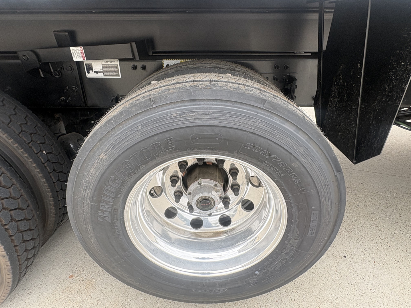 Front right wheel of a Mack GR84F dump truck showing tire branding and polished hub, with part of the chassis and fender visible.