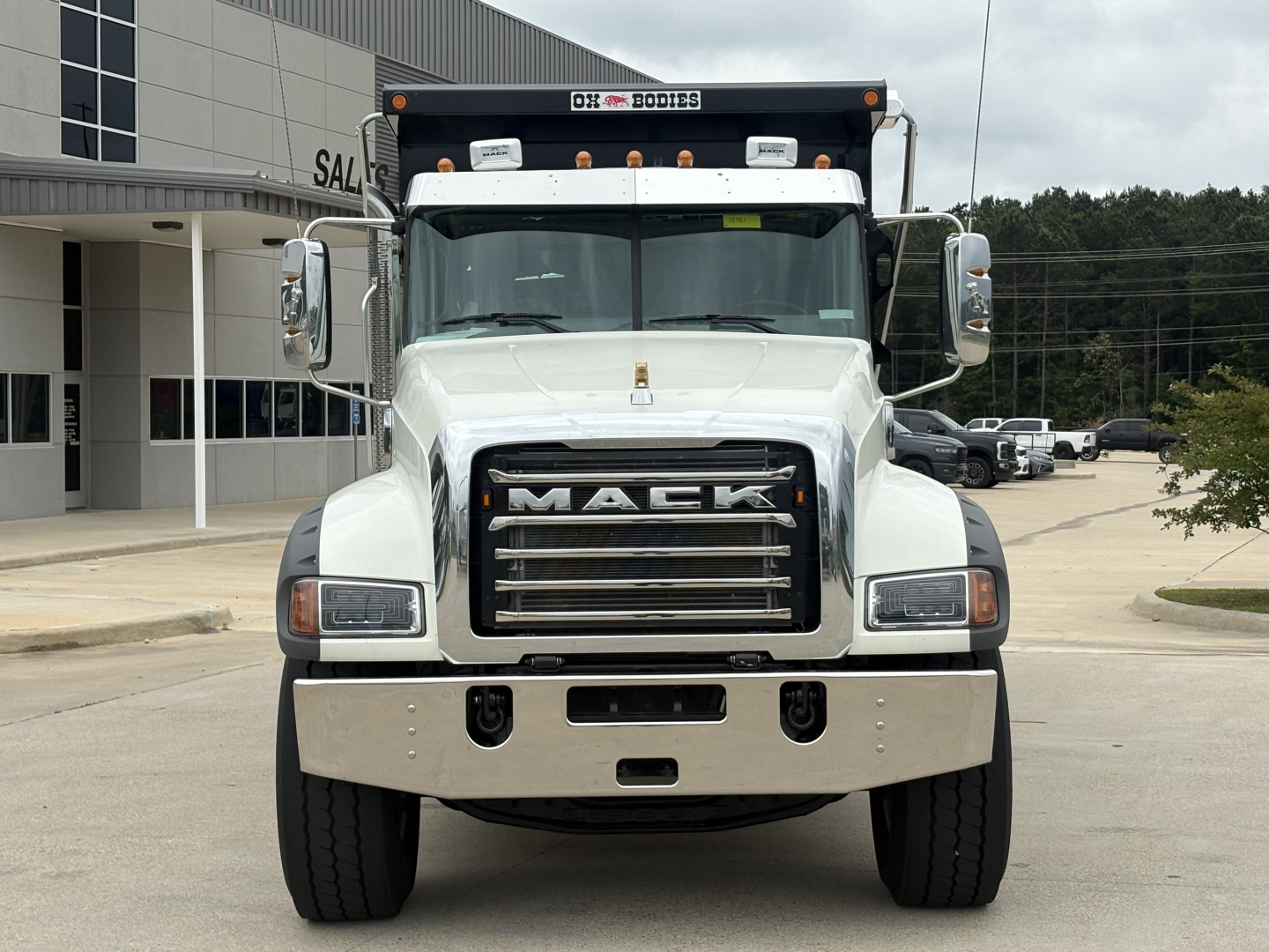 Dump truck front view of a white 2027 Mack GR84F showing grille with 'MACk' emblem and bumper, with large mirrors and roof light bar.