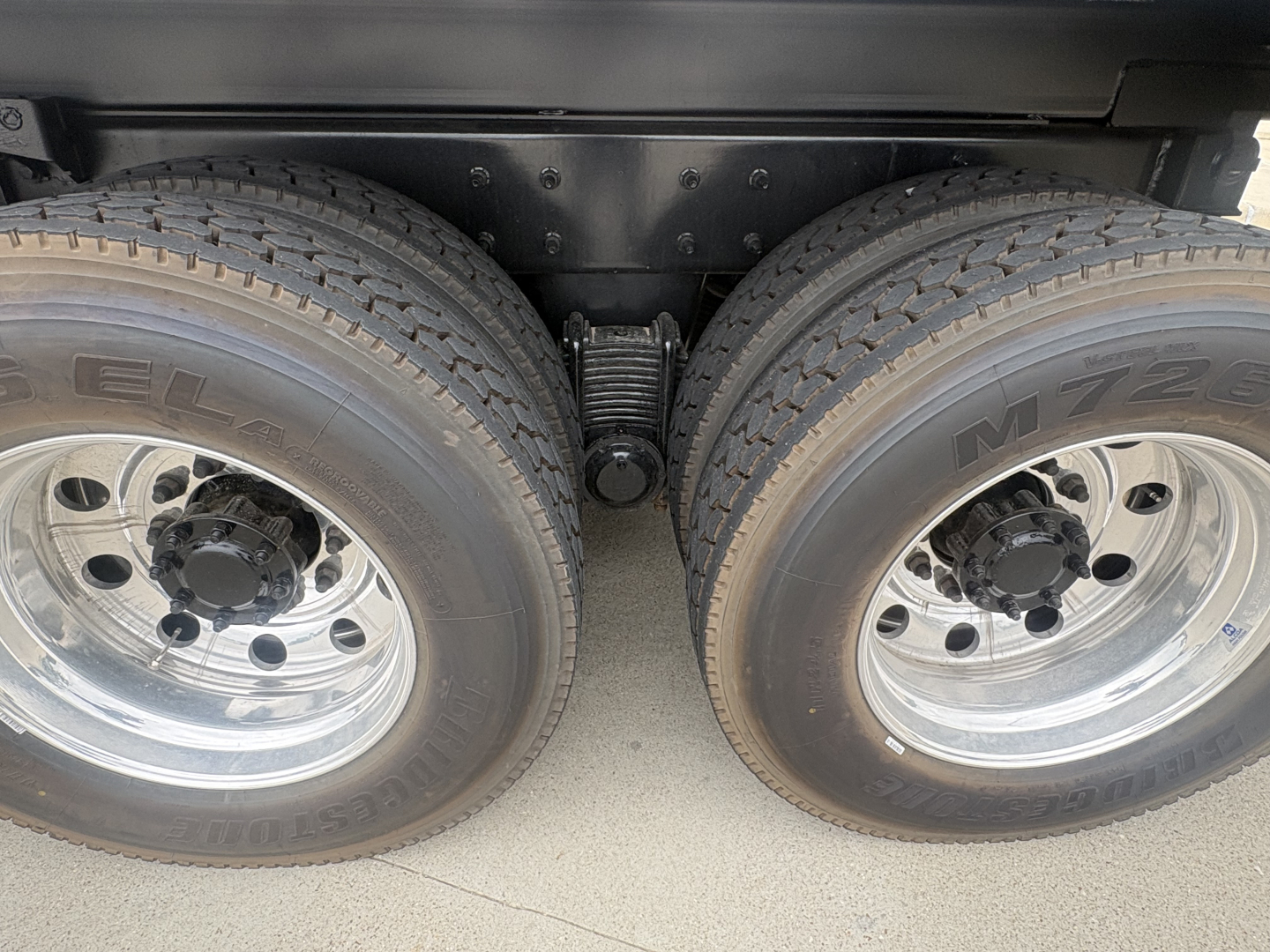 Dual rear tires on Mack heavy truck showing suspension leaf spring and differential housing.