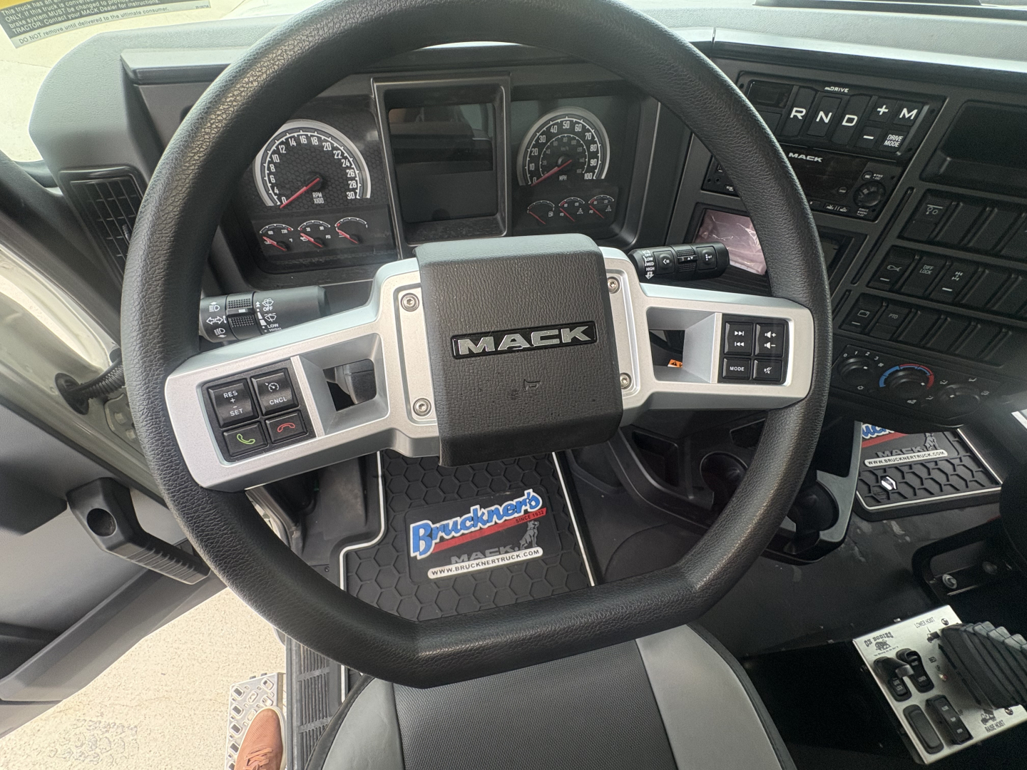 Steering wheel of 2027 Mack GR84F dump truck showing Mack emblem and dashboard controls with Buckner logo floor mat.