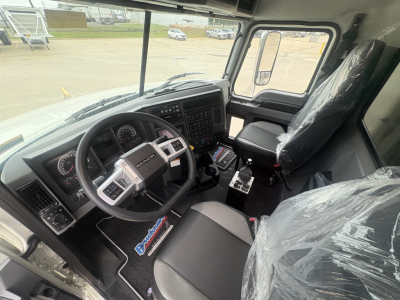 Truck cab interior of a 2027 Mack GR84F showing steering wheel, dashboard with gauges, center console, and driver seat covered in plastic.