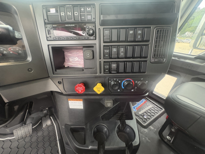 Cab interior of a Mack GR84F dump truck showing dashboard controls, gear selector, climate knobs, and cup holders.