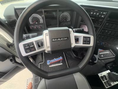 Steering wheel of 2027 Mack GR84F dump truck showing Mack emblem and dashboard controls with Buckner logo floor mat.