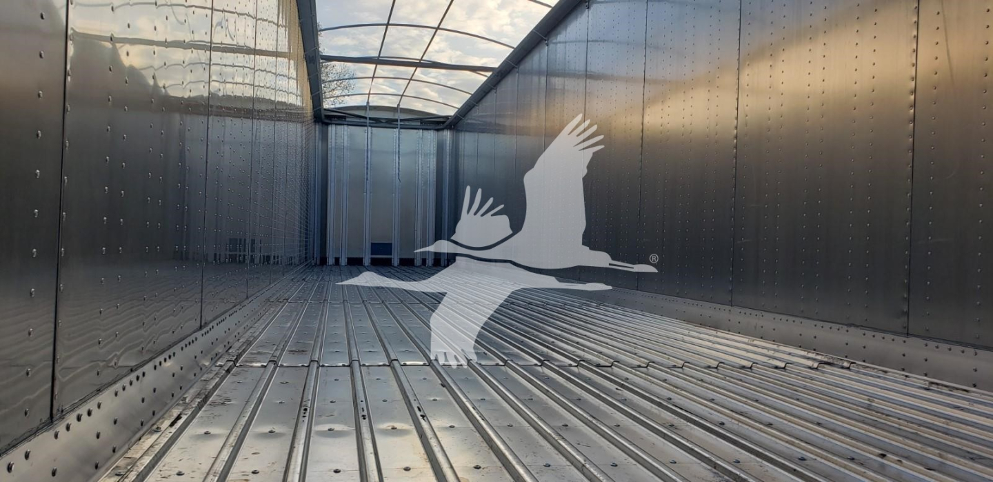 Trailer interior showing aluminum walls and floor with riveted panels, empty cargo space, logo of a flying bird overlay.