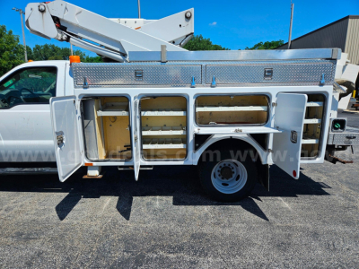 Ford F-550 service/utility truck side storage compartments open showing multiple drawers and storage bays, utility body with diamond plate tool area.