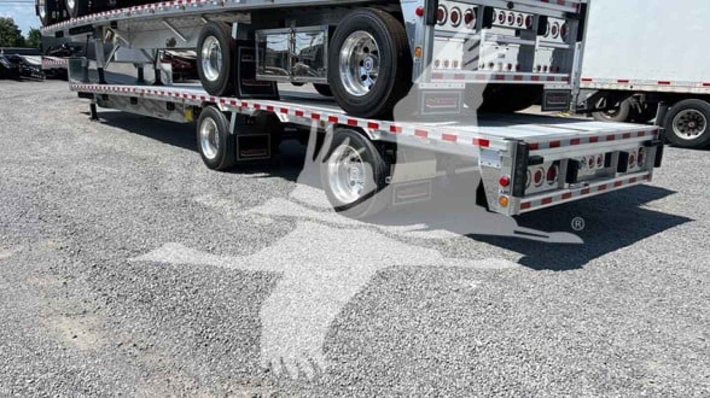 Big Bubba dropdeck trailer with multi-axle setup and rear loading ramp, chrome wheels, and polished metal surfaces.