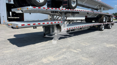 Trailer show 2026 Reitnouer Big Bubba Dropdeck flatbed with multiple levels and spare tires on rear; metal deck with reflective striping and wheels visible.