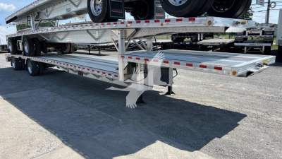 Aluminum dropdeck trailer with dual rear axles and a spare tire, visible on a portable gooseneck system, long flatbed sections, reflective red markers along the edges.