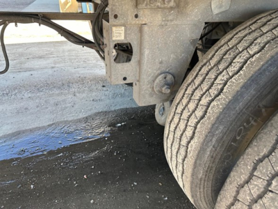 Trailer near wheel with structural hitch and tire tread, showing undercarriage and some wet pavement.
