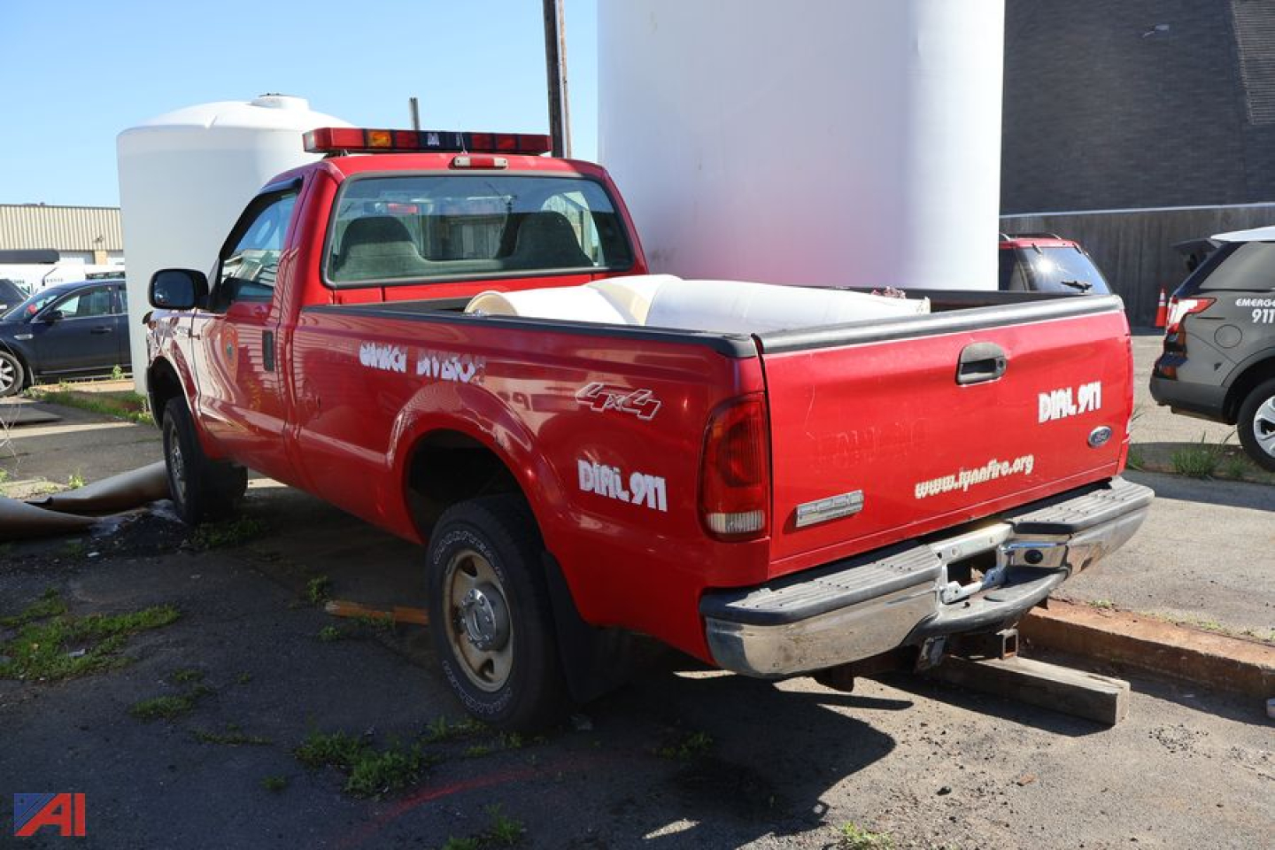 Red 2005 Ford F-250 Super Duty pickup truck with a long bed, tailgate shows DMC 911 or similar white decals and a white tank in the bed. Rear view with bumper and taillights visible.