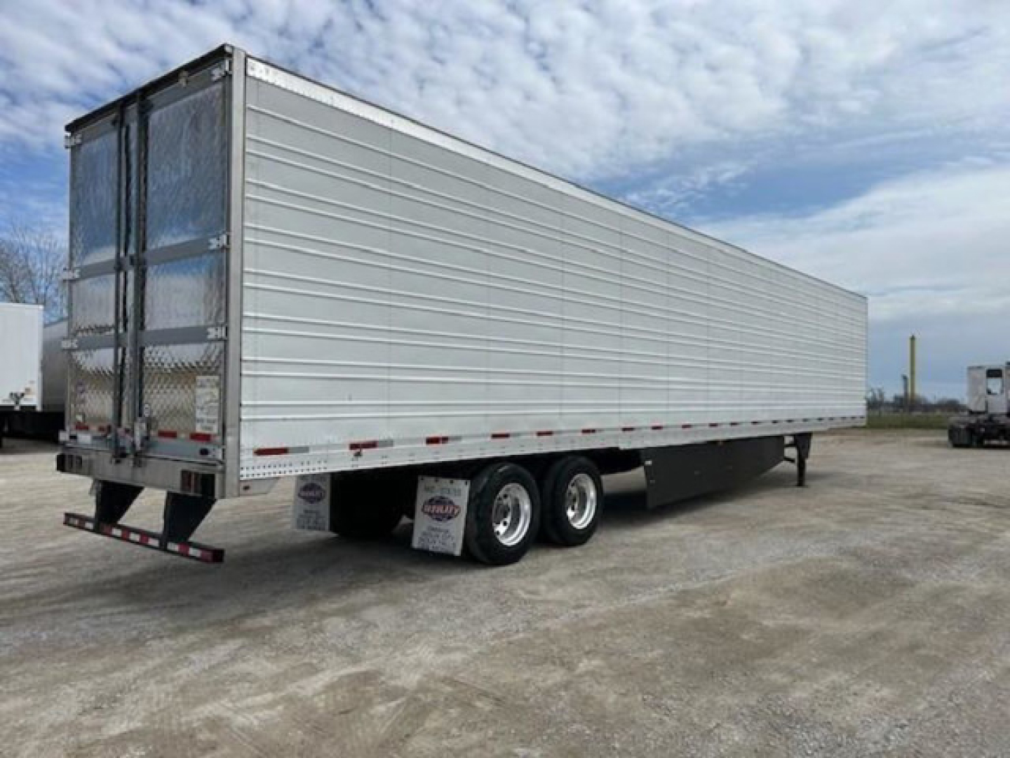 Utility refrigerated trailer viewed from side-rear showing tandem axles and metal exterior with doors at back.