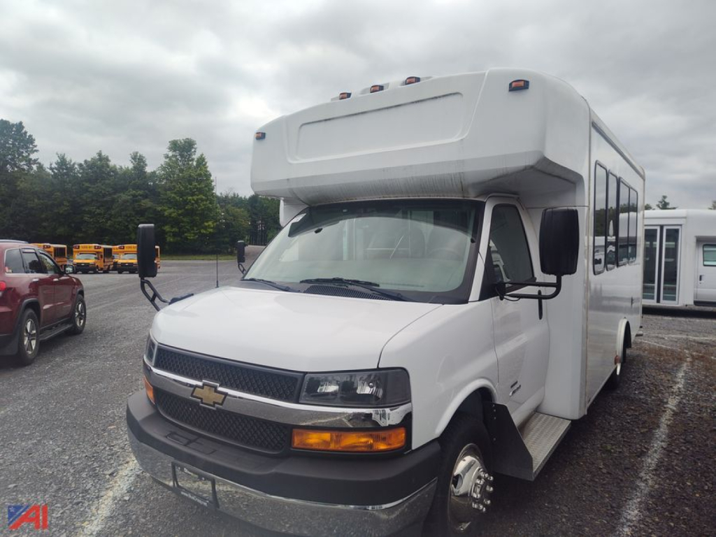 Bus front/side view showing Chevrolet Express G4500 bus body with cab-over styling, white exterior, black grille, amber turn signals, and side mirrors.