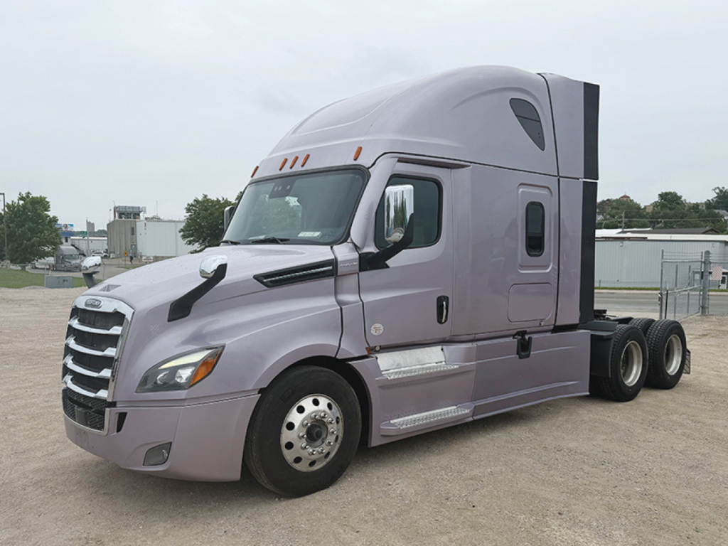 Truck cab exterior side view showing 2023 Freightliner Cascadia126 in lavender color, sleeper cab with aerodynamic fairing, tandem rear axles, front grille, and side steps.
