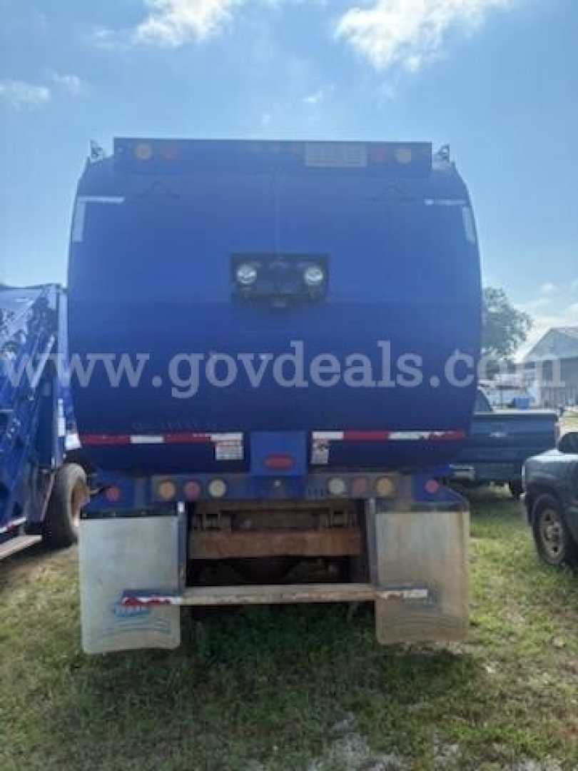Rear view of a blue garbage truck bin mounted on a chassis with dual rear mud flaps and warning lights; there is a watermark from govdeals on the image.