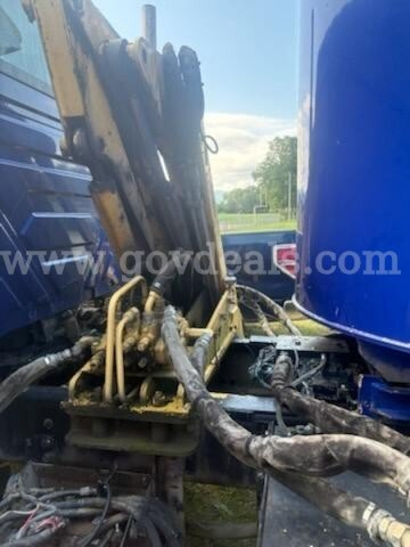 Truck hydraulic lines and hydraulic arm visible between a blue cab and a yellow lifting mechanism.
