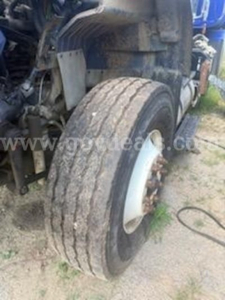 Truck front wheel assembly showing large dual-tire with dirty tread and exposed brake rotor; fender and undercarriage components visible.