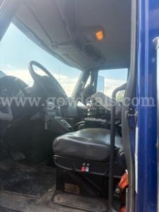 Truck cab interior of a 2011 International 7500, front seats and steering wheel visible, dashboard area, driver’s seat with gray upholstery, overhead light, windshield and side door frame.