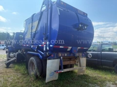 Garbage truck rear view showing blue body, rear bumper, and hydraulic compactor with a white mudguard; stock number and watermark visible.