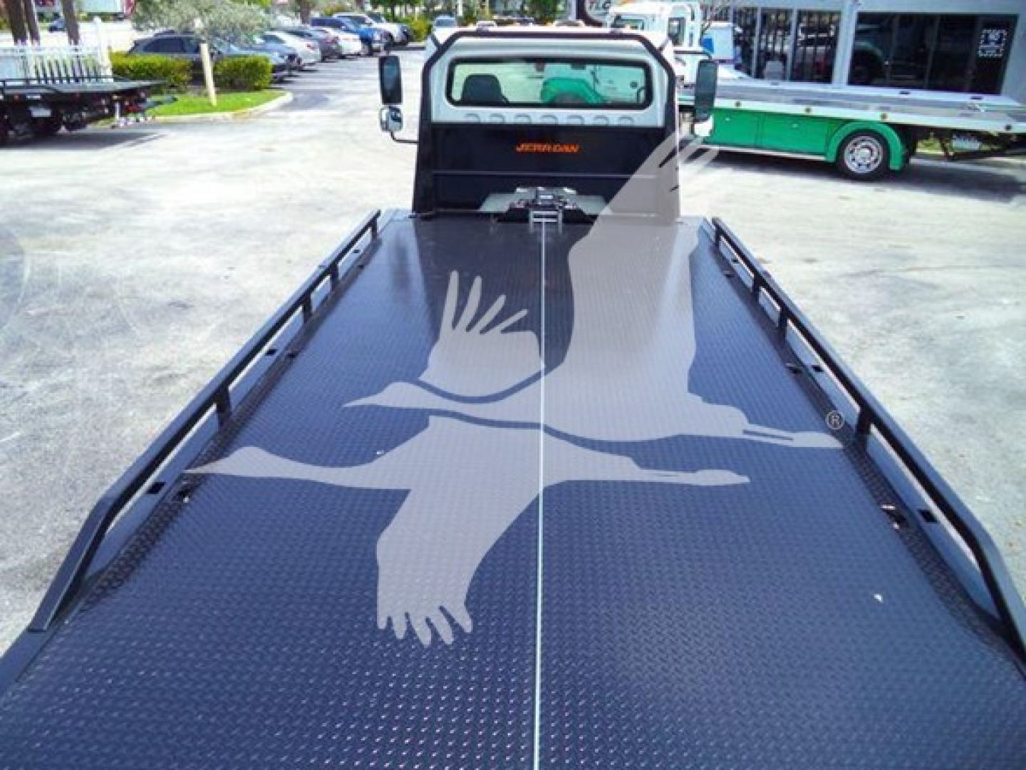 Flatbed truck with a long diamond plate bed and side rails, seen from the rear cabin area; Freightliner Jerr-Dan logo on cab.
