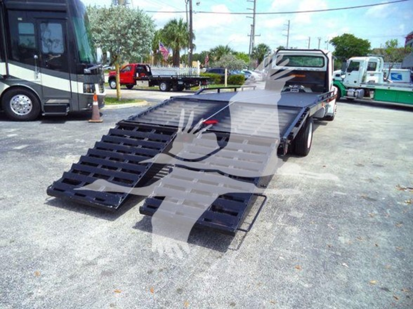 Flatbed tow truck with lowered ramp in a truck lot showing a Freightliner Business Class M2 106 bed and ramps.