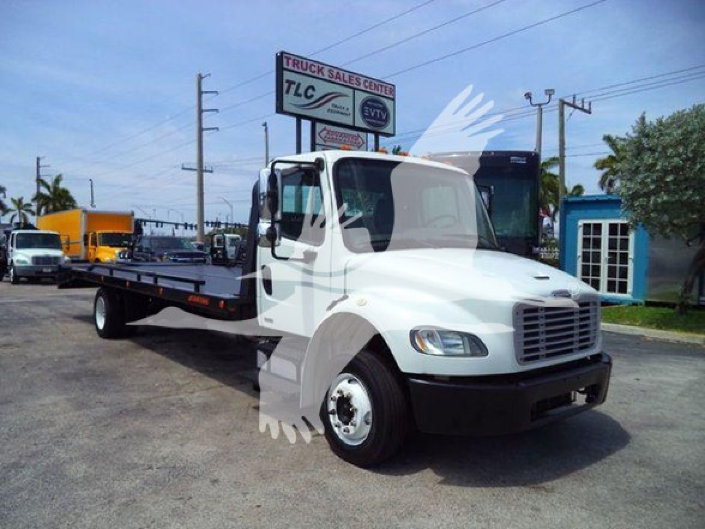 Flatbed tow truck 2012 Freightliner Business Class M2 106 with white cab and black front bumper, operating in a dealership lot.
