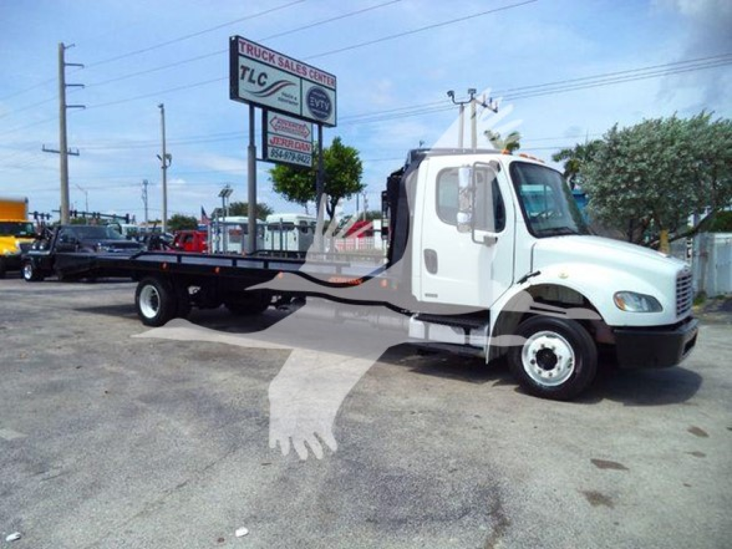 Freightliner Business Class M2 106 flatbed truck side view showing cab and long flatbed, white truck in a lot with dealership signs