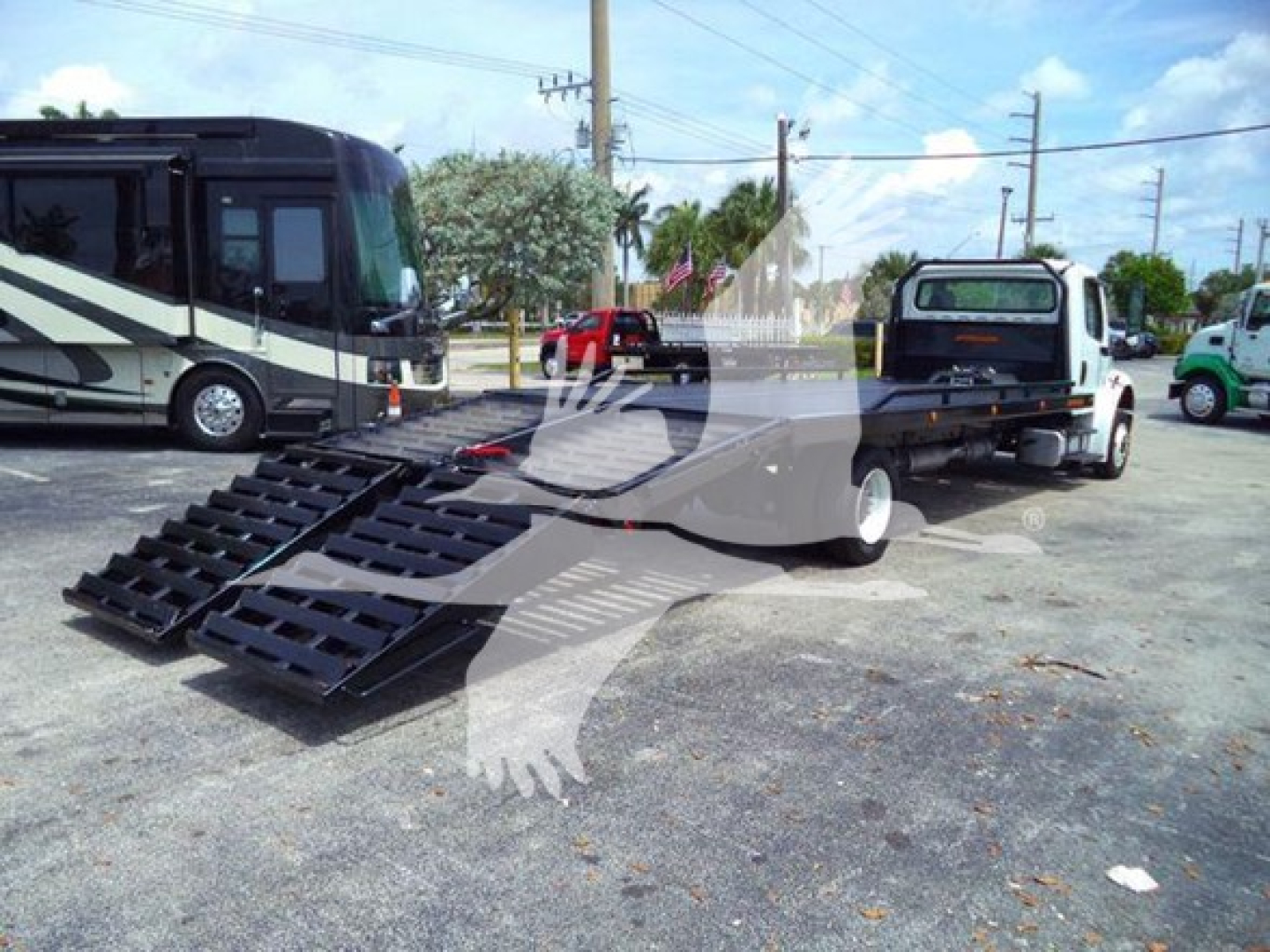 Flatbed tow truck with a ramp on the ground, Freightliner Business Class M2 106 in background, VIN 1FVACWDT1CHBP9505, stock TBP9505, category flatbed.
