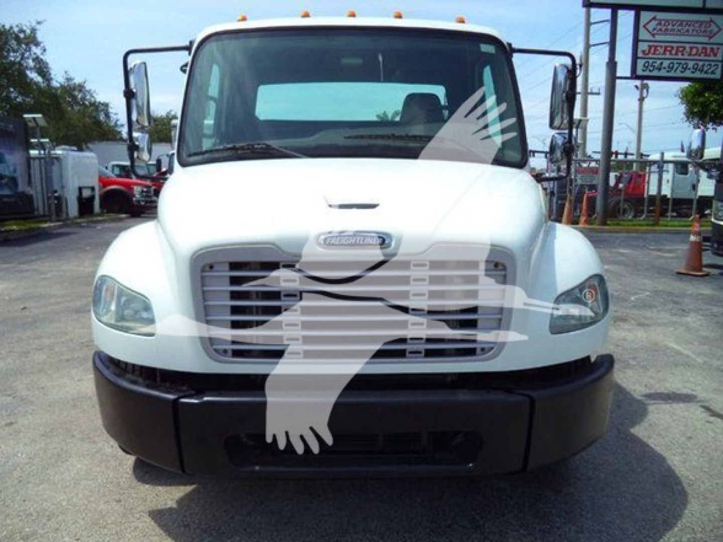 Front view of a 2012 Freightliner Business Class M2 106 flatbed truck showing grille and bumper, with headlights and windshield visible.