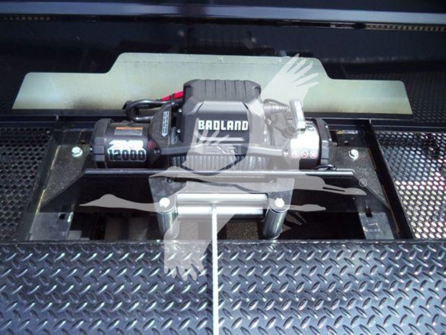 Winch mounted on diamond plate bed with Badland winch brand and 12000 label visible