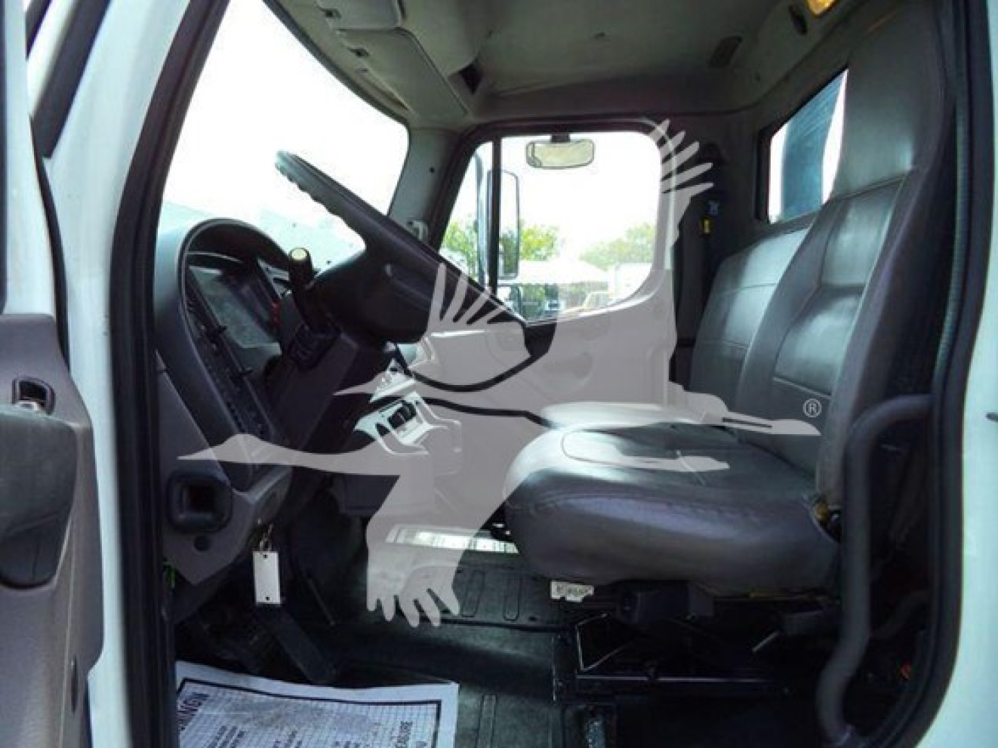 Cab interior of a 2012 Freightliner Business Class M2 106 flatbed truck showing driver seat, steering wheel, and dashboard.