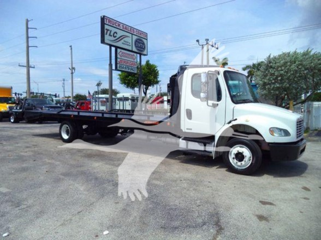 Freightliner Business Class M2 106 flatbed truck side view showing cab and long flatbed, white truck in a lot with dealership signs