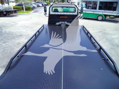 Flatbed truck with a long diamond plate bed and side rails, seen from the rear cabin area; Freightliner Jerr-Dan logo on cab.