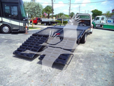 Flatbed tow truck with lowered ramp in a truck lot showing a Freightliner Business Class M2 106 bed and ramps.