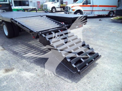 Flatbed truck chassis with fold-out loading ramps and gooseneck hitch area visible.