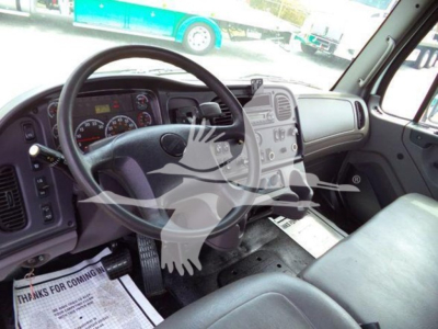 Cab interior of a Freightliner Business Class M2 106 showing steering wheel, dashboard, and driver seat with pedals visible.