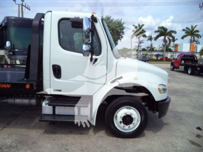Freightliner Business Class M2 106 flatbed truck side view showing front cab and wheel; white cab, side steps, and flatbed equipment visible.