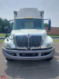 Truck front view showing large chrome grille and International emblem, box truck cab with side mirrors and elevated sleeper, white paint, bumper details.