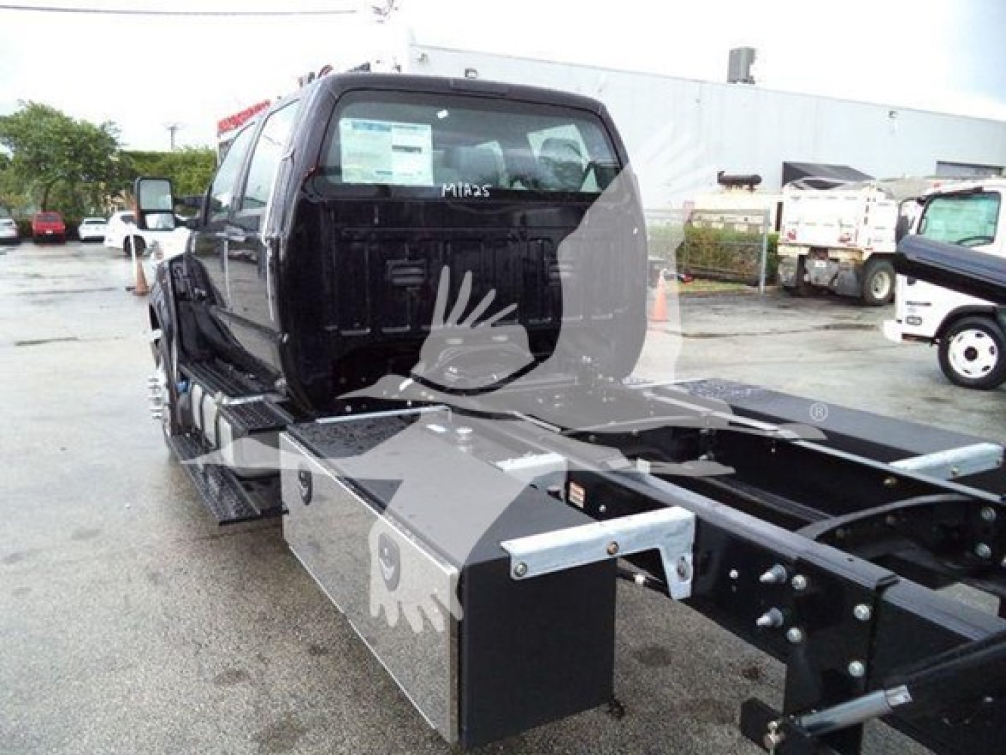 Ford F-750 rollback truck cab and chassis view showing rear cab, bed mounting rails, and side storage box with metal toolbox.