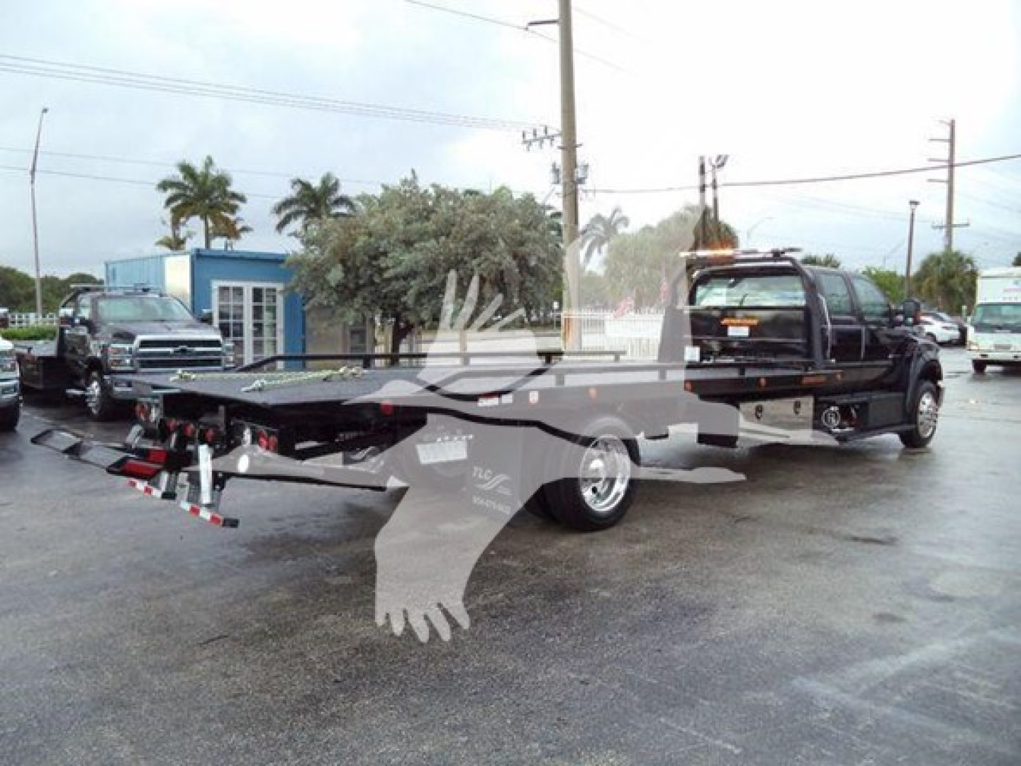 Ford F750 tow truck rollback bed with wheel lift and towing equipment visible, side view showing cab and flatbed.