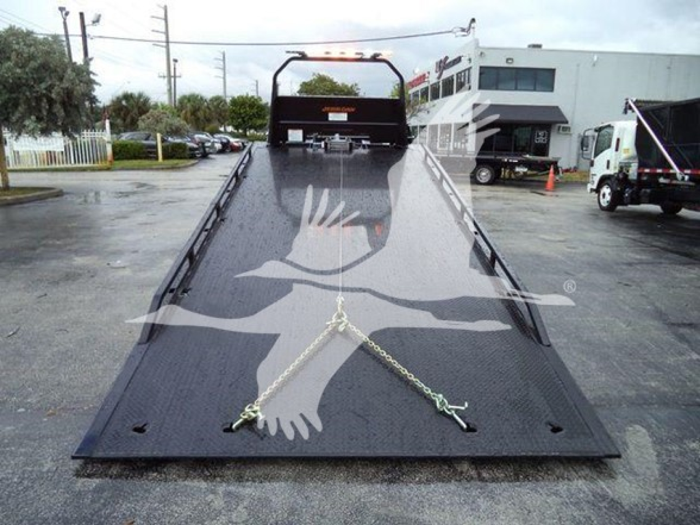 Ford F750 rollback truck deck with ramp in lowered position and safety chains, front winch area visible.