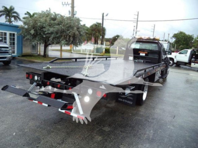 Flatbed tow truck chassis with extended bed and rear ramps, Ford F-750 rollout truck in a dealership lot.