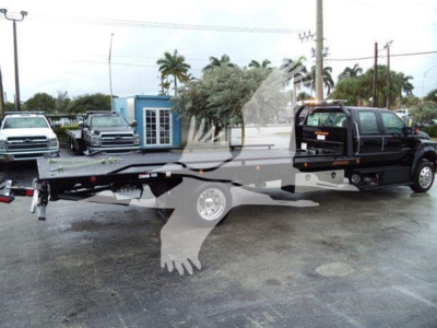 Flatbed rollback tow truck in a dealership lot showing a Ford F750 chassis with extended flatbed and tow wheel lift. Visible text not legible due to watermark.