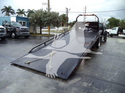 Flatbed tow truck with a large metallic loading ramp in a dealership lot.