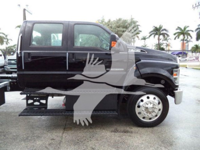 Ford F-750 rollback truck side view showing black cab and dual rear wheels with chrome hubcaps, side step, and branding on front fender.