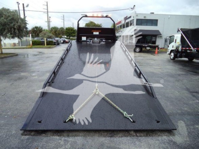 Ford F750 rollback truck deck with ramp in lowered position and safety chains, front winch area visible.