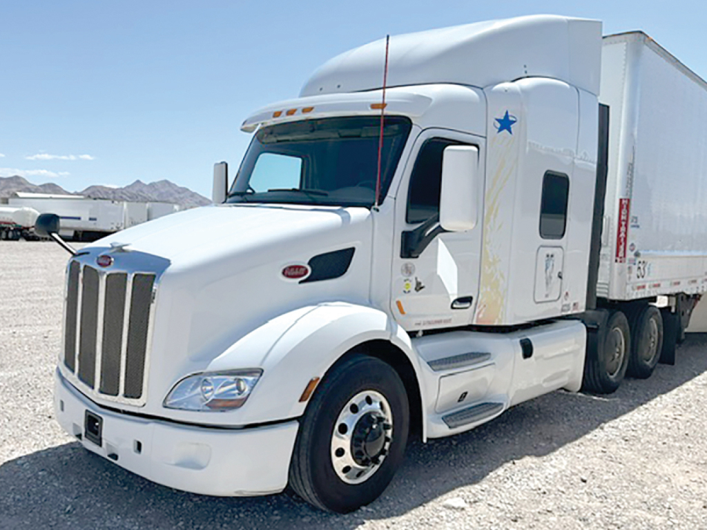 Peterbilt 579 UltraCab tractor with white Sleeper, chrome grille, side window, blue star decals, attached white box trailer, VIN and stock not visible on exterior.
