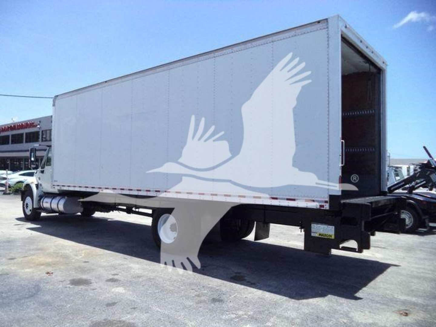 Box truck with white cargo area and trailer hitch showing logo on side; clear side view with rear open bay and box truck chassis.