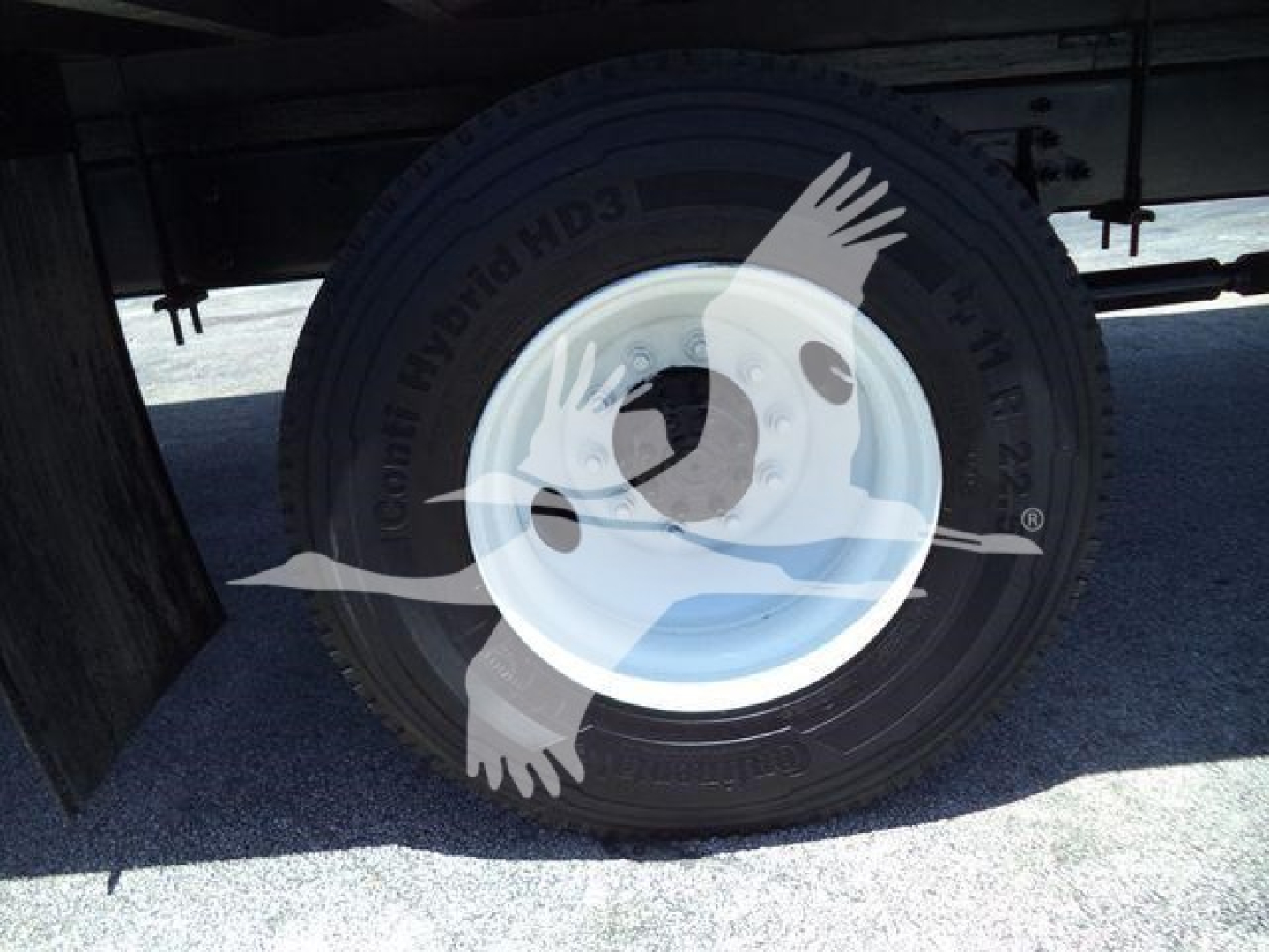 Truck tire and wheel under a box truck showing a rugged tire with white rim and sidewall labels.