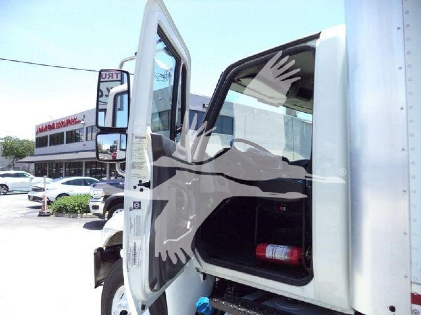 Truck cab interior and front door open showing storage area and a fire extinguisher; side mirror and part of box truck body visible.